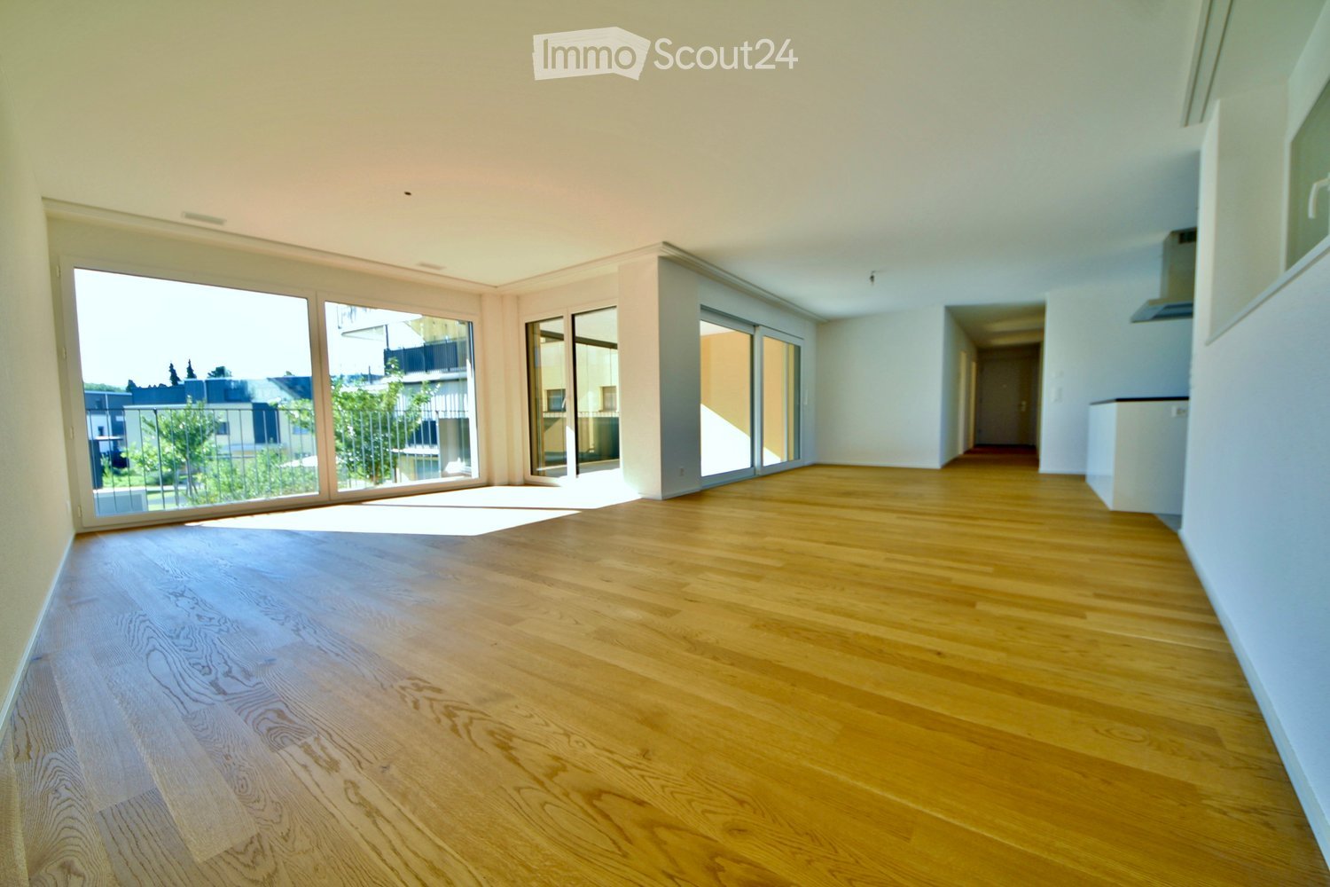 Empty room with light wooden flooring, large glass sliding doors leading to a balcony, and white walls.