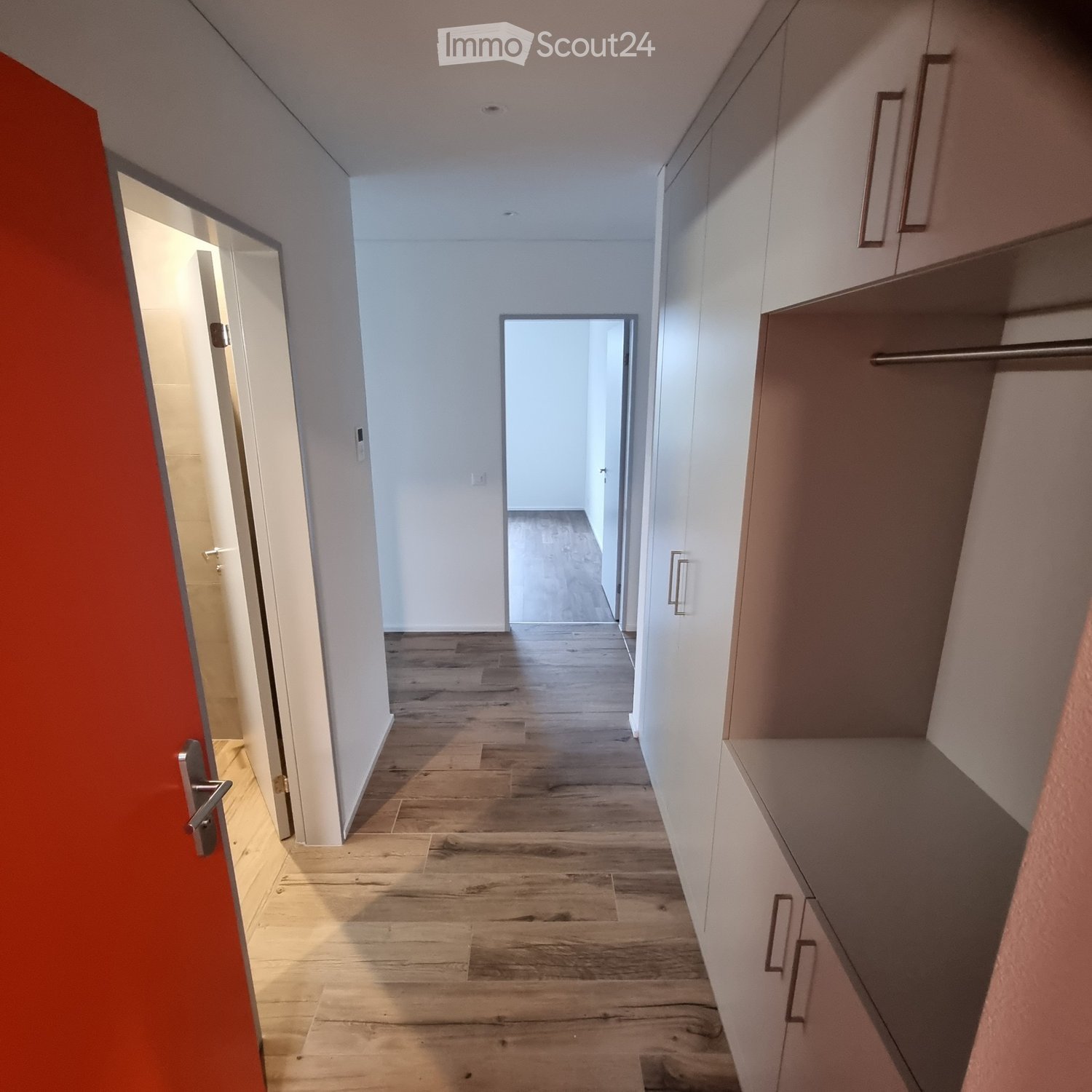 Empty hallway with wooden flooring, white walls, and built-in storage units on one side. Two doors are visible, one leading to another room.