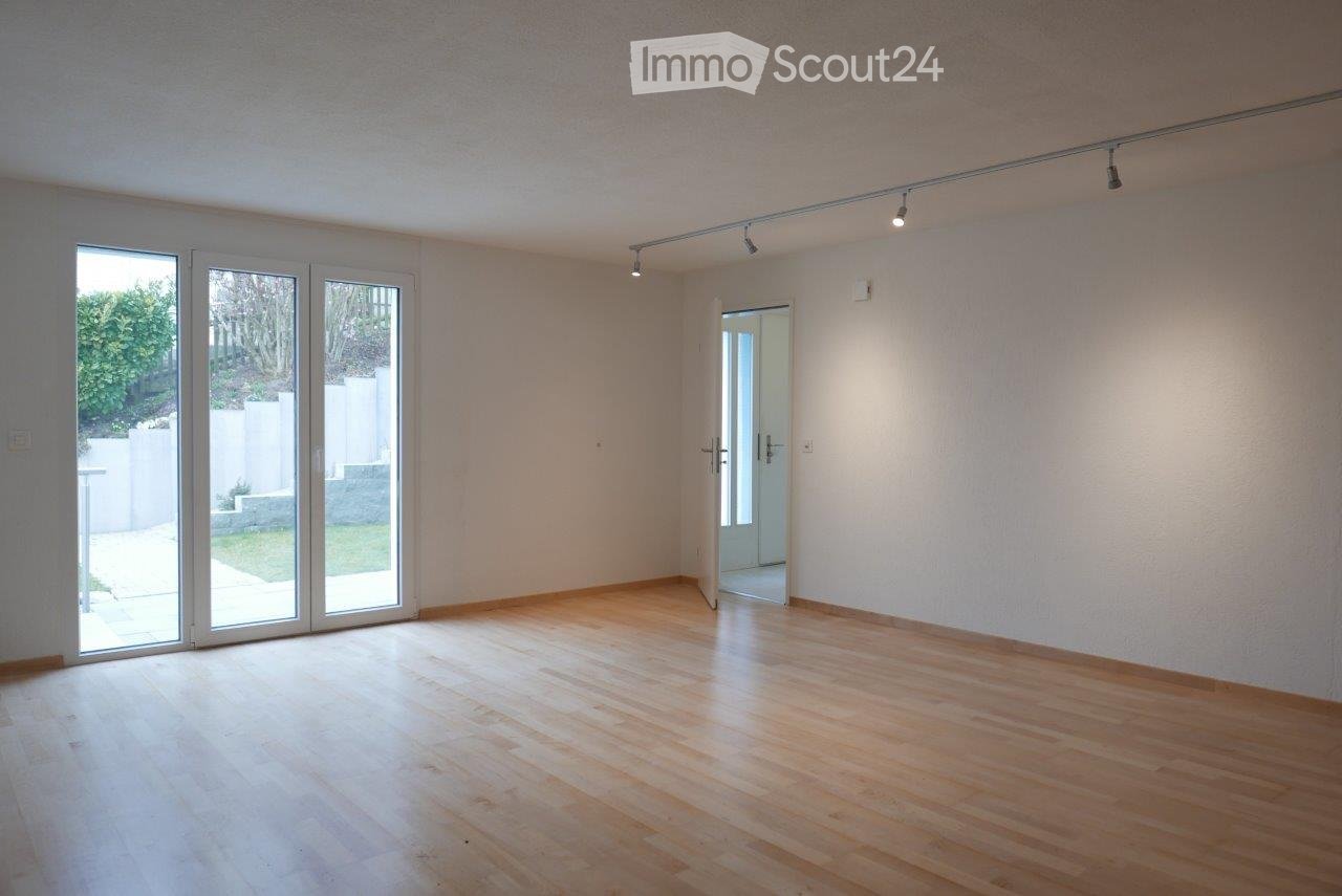 Empty room with light wooden flooring, white walls, large glass sliding doors leading to an outdoor area, and recessed lighting.