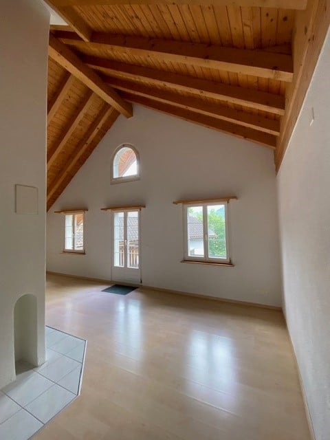 Bright, empty room with wooden beams on the ceiling, large windows, and a tiled floor. No furniture or equipment present.