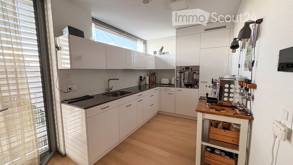 Modern kitchen with white cabinets, black countertops, wooden island, coffee machine, and large window with blinds.
