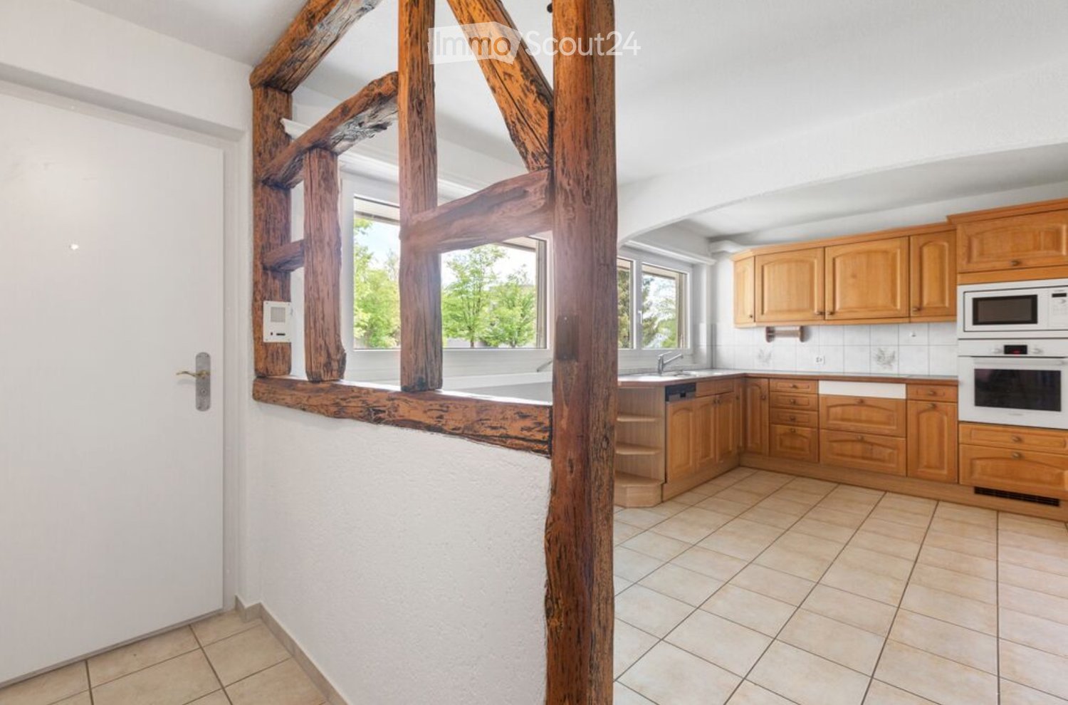 Bright kitchen with wooden cabinets, microwave, oven, sink, and faucet. Exposed wooden beams and tiled floor.