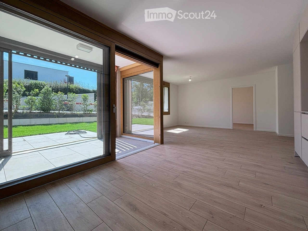 Empty room with wooden flooring, large sliding glass doors leading to a patio, white walls, and minimal lighting.