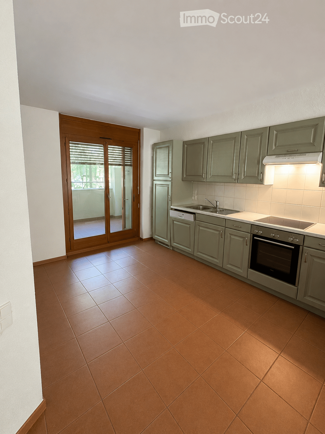 Modern kitchen with grey cabinets, stainless steel appliances, and a large sliding glass door leading to a balcony.