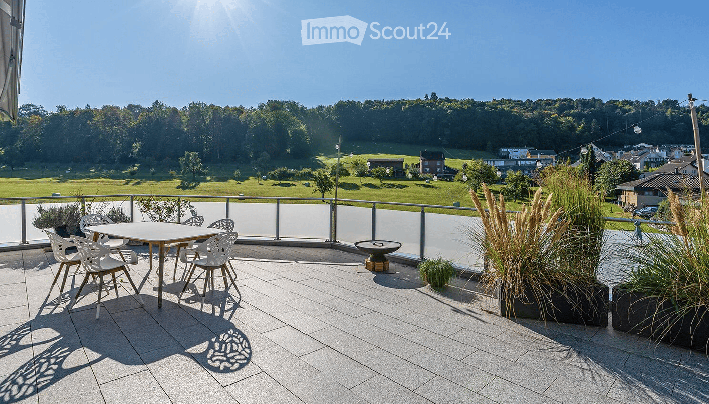Balcony with a table and chairs, surrounded by greenery and a scenic view of a park and town.