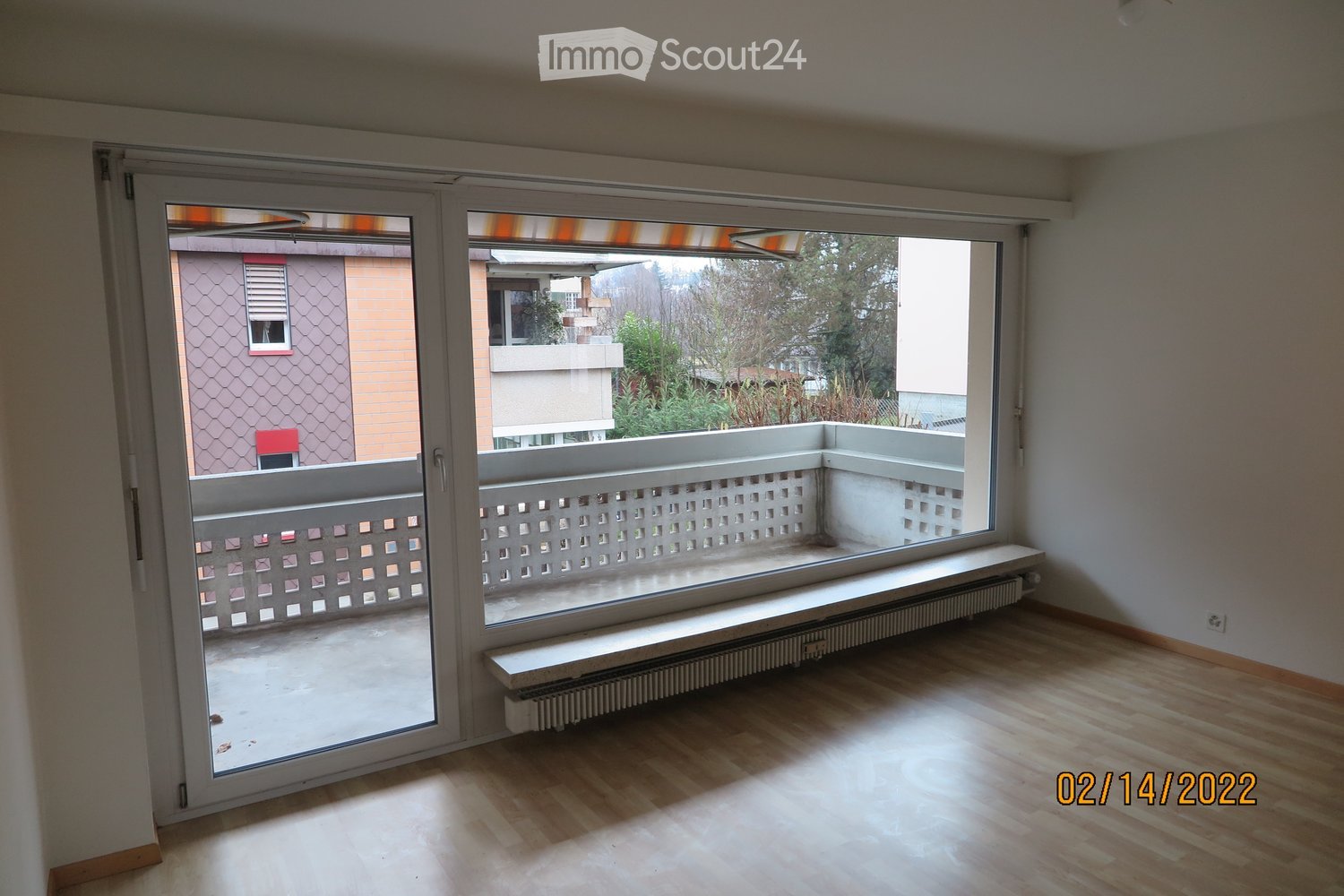 Empty room with wooden flooring, large windows, radiator, and sliding glass doors leading to a balcony.