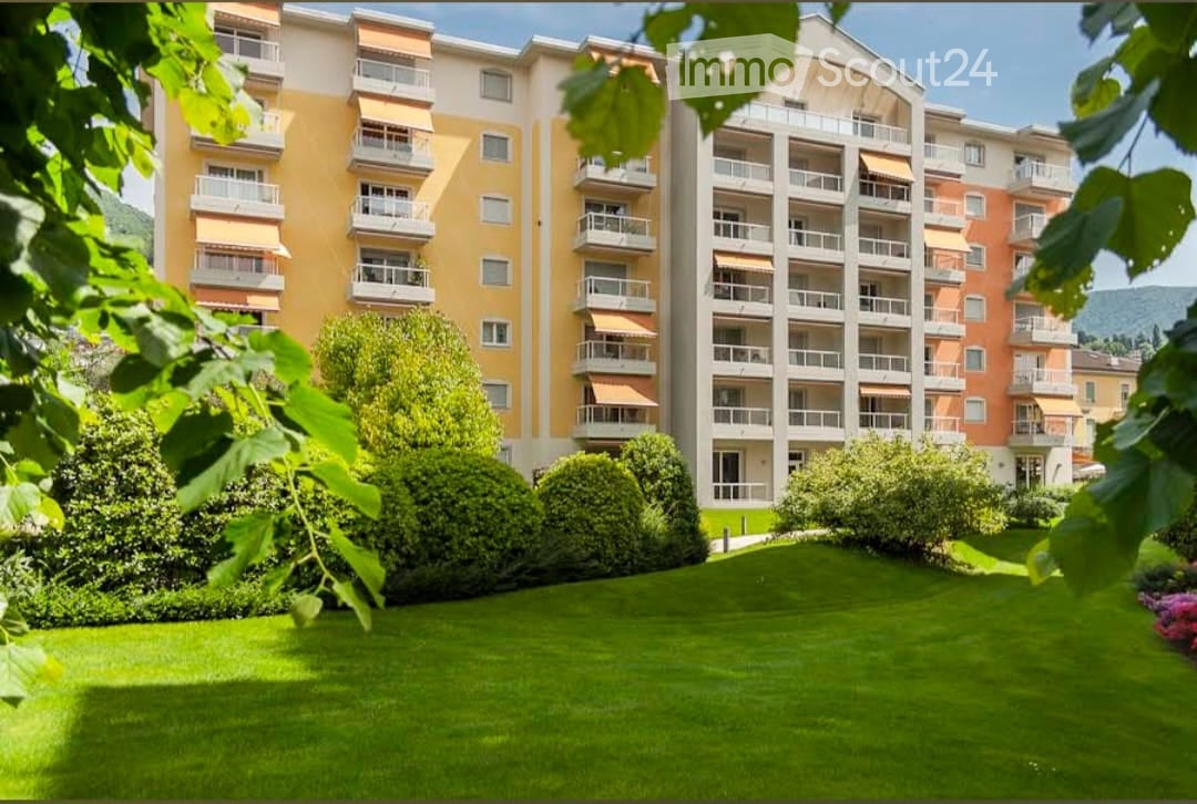 Multi-story residential building with balconies, surrounded by a well-maintained lawn and trees.