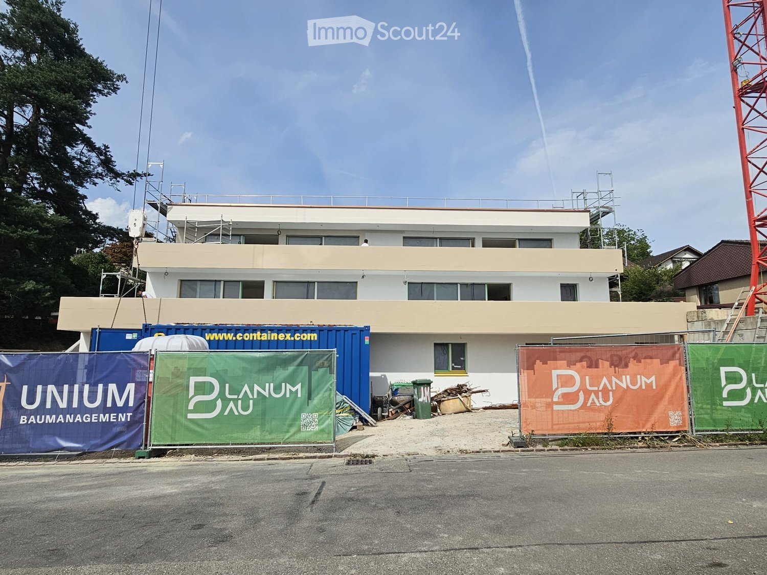 Modern two-story building under construction with scaffolding, banners, and construction materials visible.