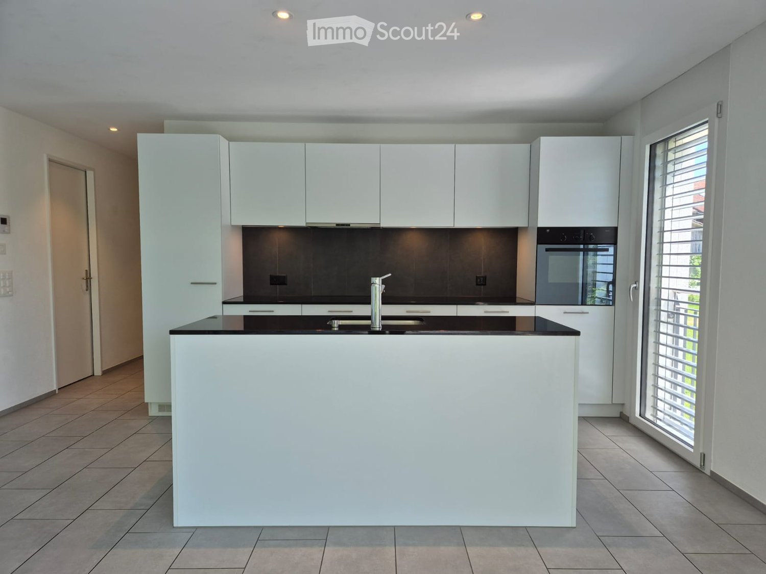 Modern kitchen with white cabinets, black countertops, a central island, and built-in appliances including an oven and sink.