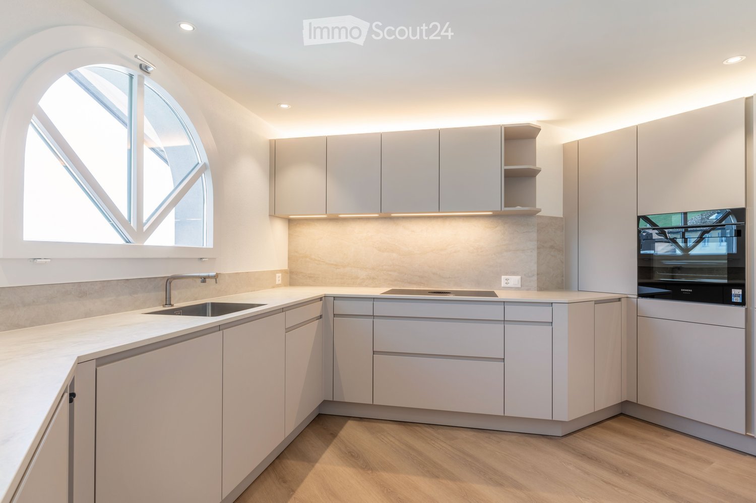 Modern kitchen with white cabinets, marble countertop, stainless steel sink, and built-in oven.