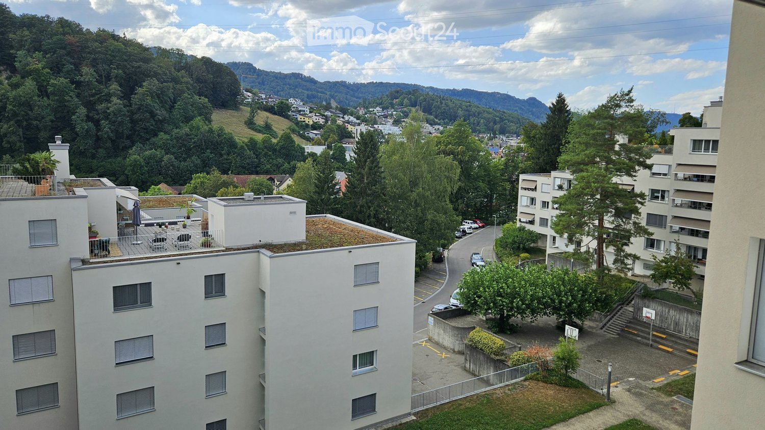 View from a rooftop terrace showing multiple apartment buildings, green hills, and a town in the distance.