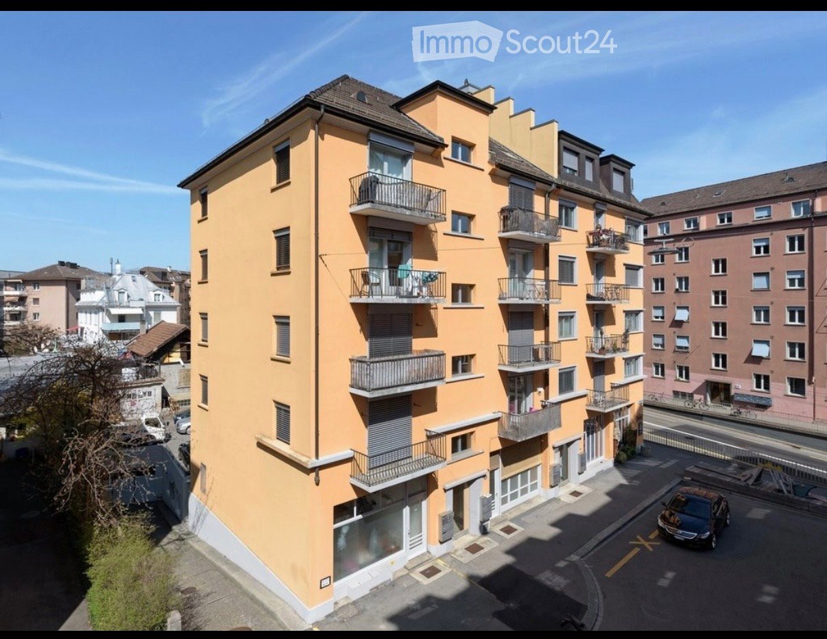Multi-story residential building with yellow facade, multiple balconies, and surrounding urban environment.