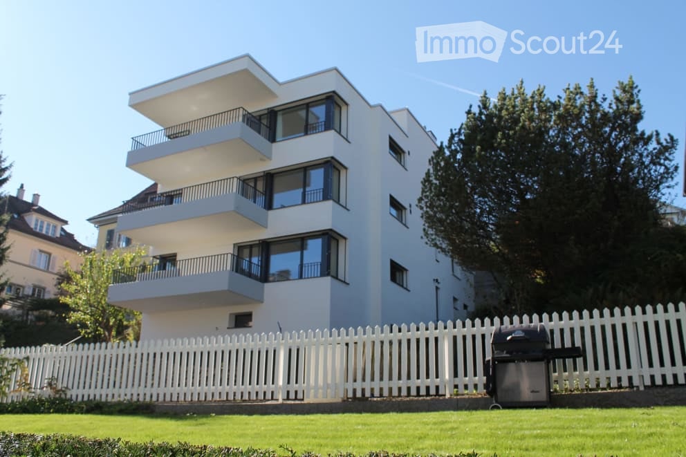 Modern multi-story apartment building with white exterior, large windows, and multiple balconies.