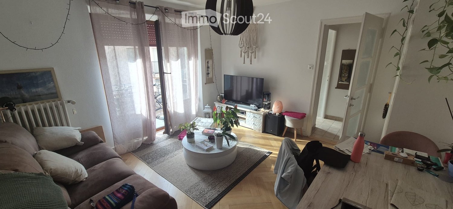 Bright living room with wooden flooring, large windows, balcony access, sofa, coffee table, TV, and plants.