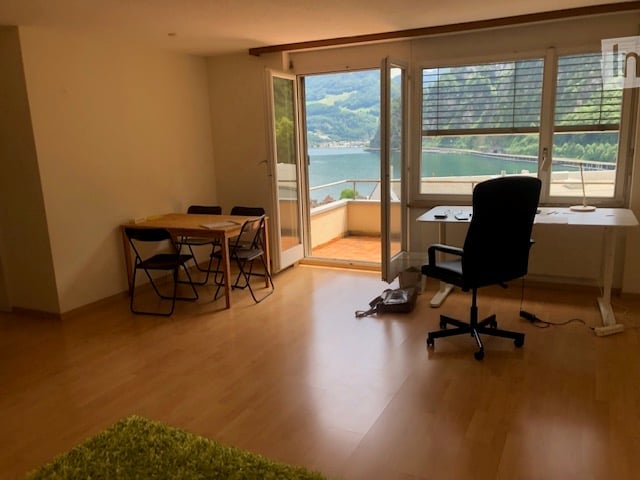 Bright room with wooden flooring, large windows offering a scenic view, a dining area with a table and chairs, and a workspace with a desk and chair.