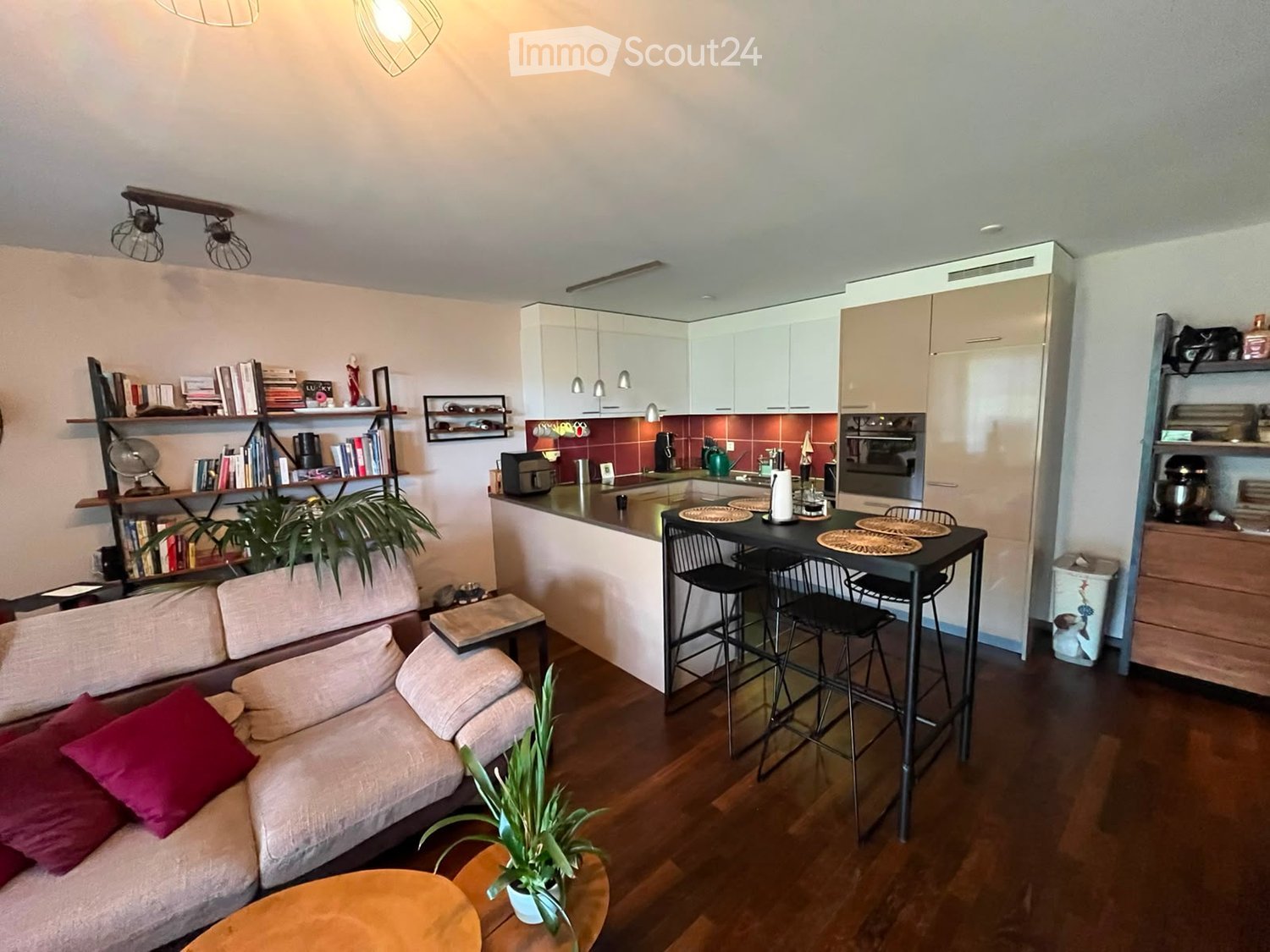 A modern, open-concept living and dining area with a sofa, coffee table, dining table, and kitchen appliances.
