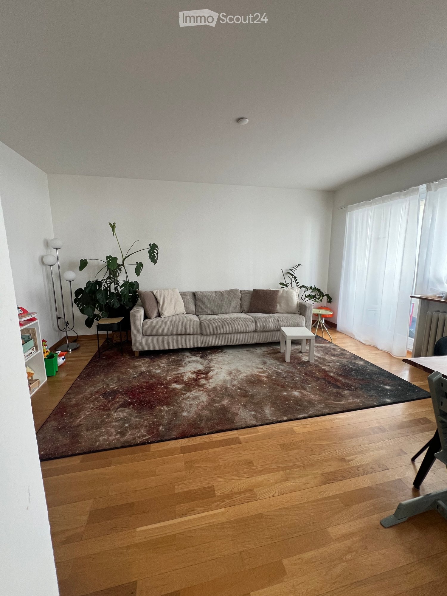 Living room with wooden flooring, large sofa, coffee table, side tables, floor lamp, and plants.