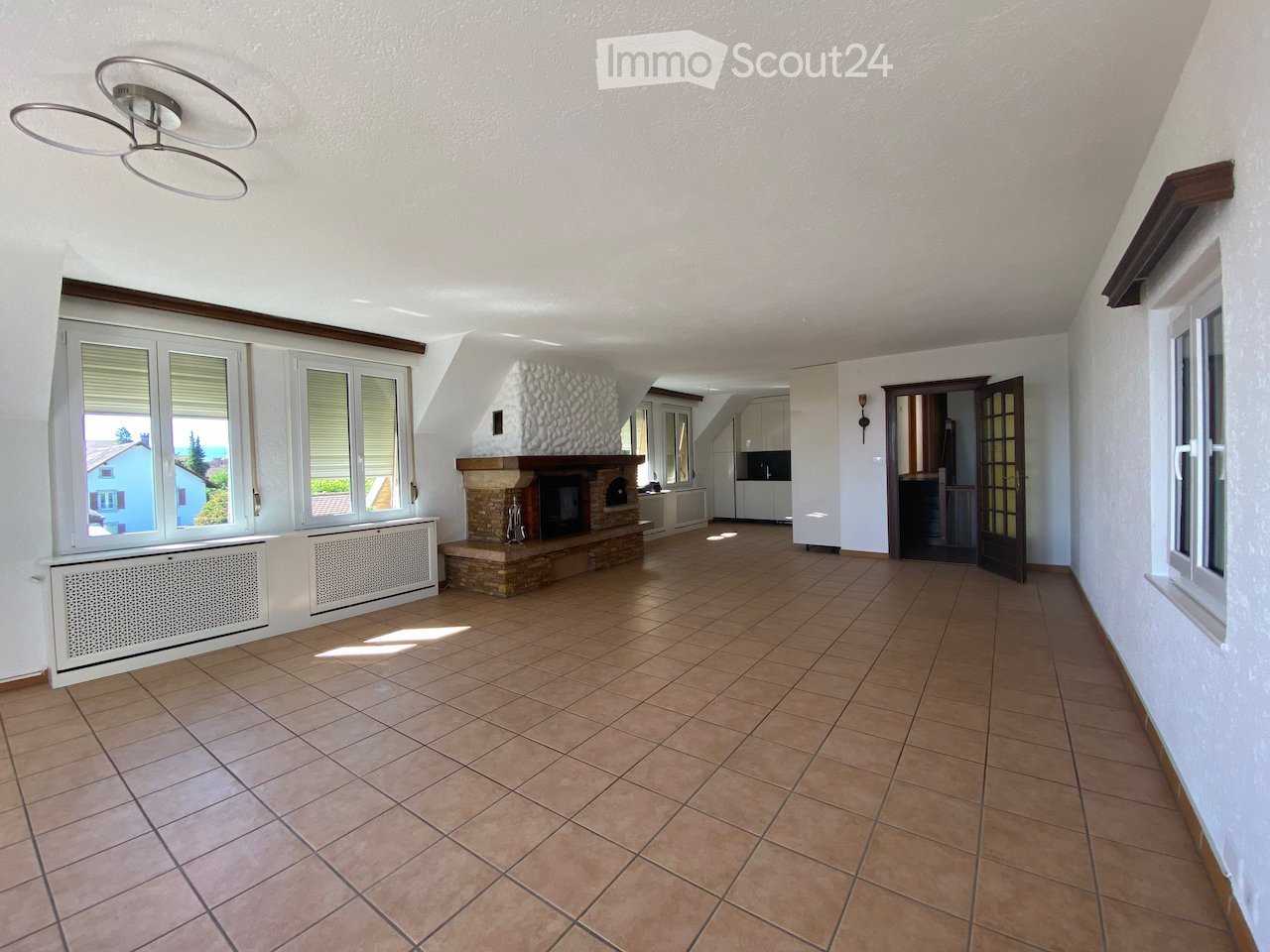 Bright hallway with tiled floor, large windows, fireplace, and open doorway leading to another room.
