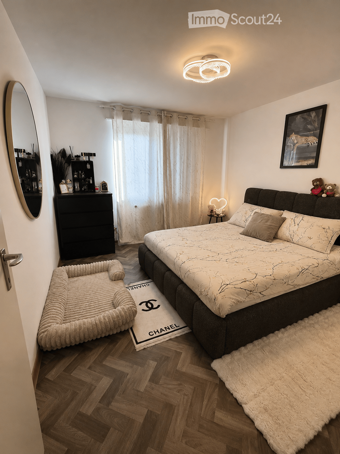 Modern bedroom with a large bed, nightstand, mirror, dresser, picture frame, dog bed, and a fluffy rug.