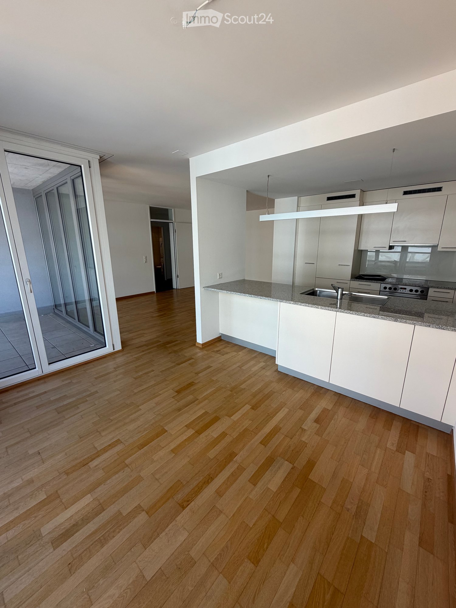 Empty room with wooden flooring, white kitchen cabinets, and a large sliding glass door leading to a balcony.