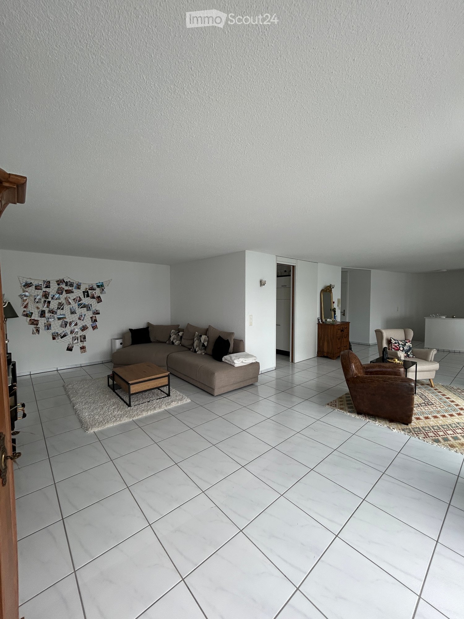 Bright living room with white walls, tiled floor, and modern furniture including a sofa, coffee table, and chairs.