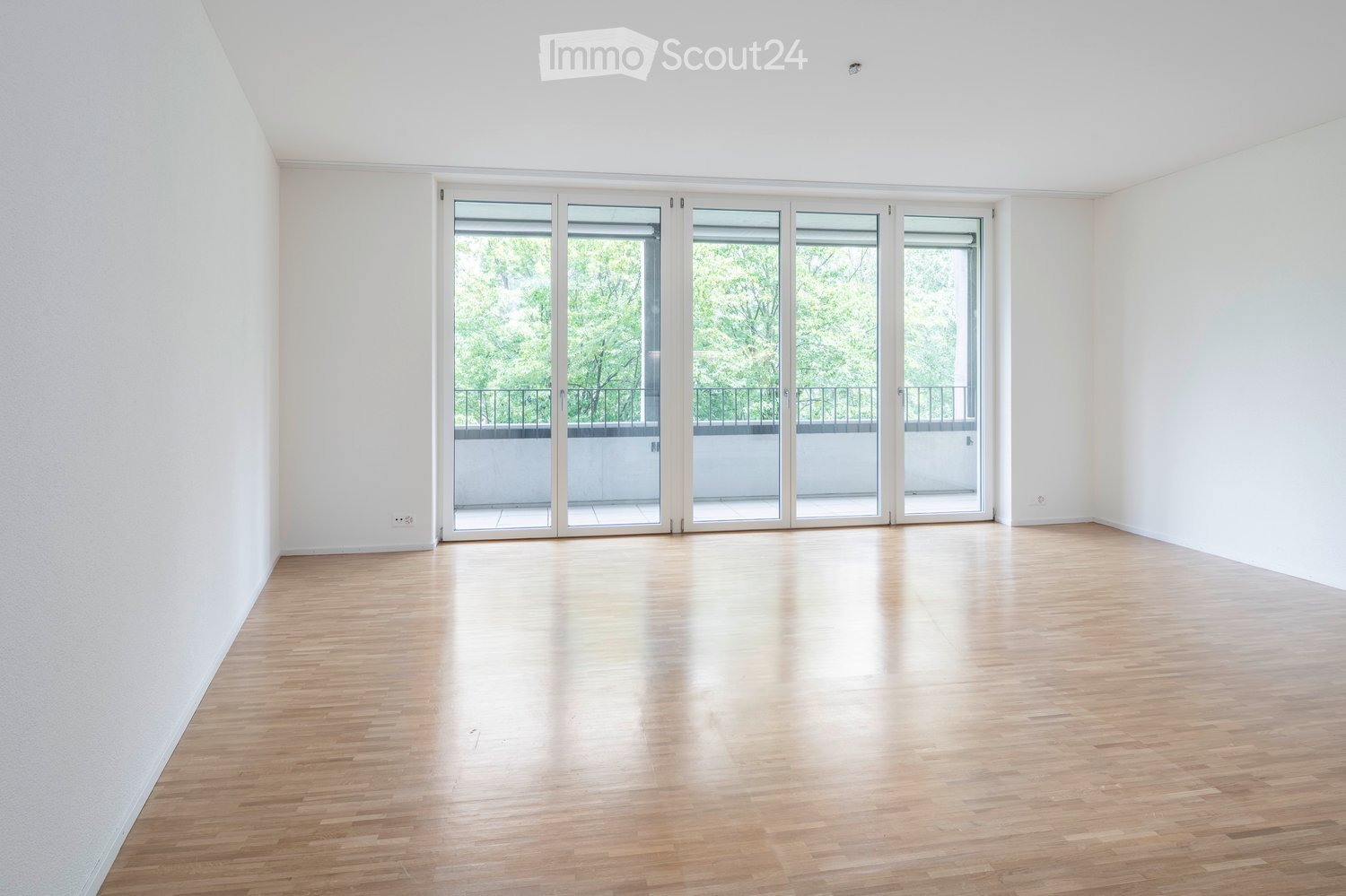 Empty room with wooden flooring, white walls, and large sliding glass doors leading to a balcony.