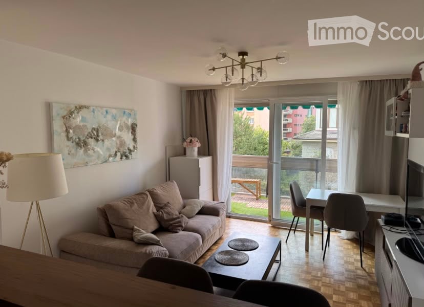 A modern, open-concept living and dining area with a sofa, coffee table, dining table, chairs, and a balcony with outdoor furniture visible through large glass doors.