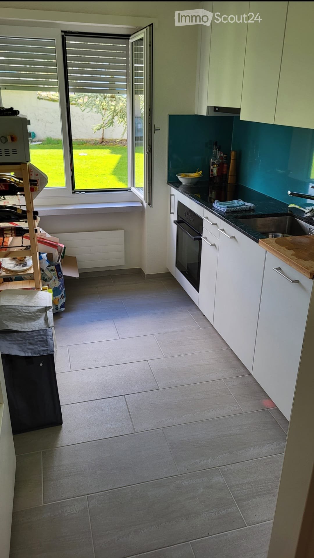 Modern kitchen with white cabinets, dark countertops, and a tiled floor. Features an oven, sink, and various kitchen items on the counter.