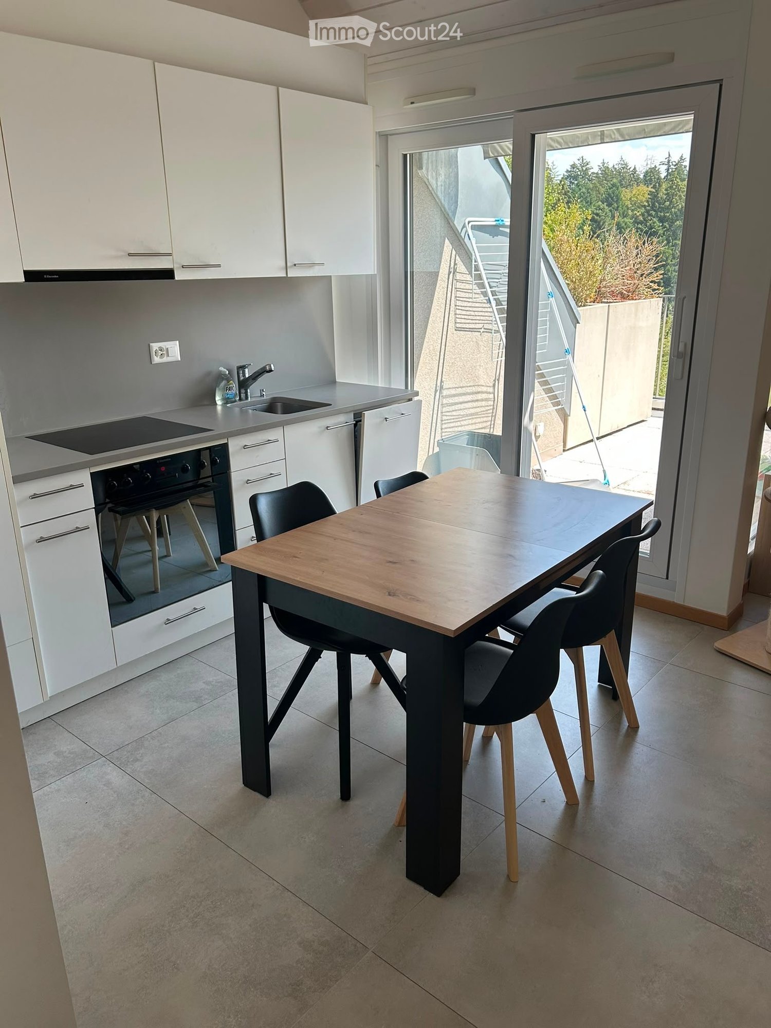 Modern kitchen with white cabinets, a wooden dining table, black chairs, and built-in appliances including an oven and sink.