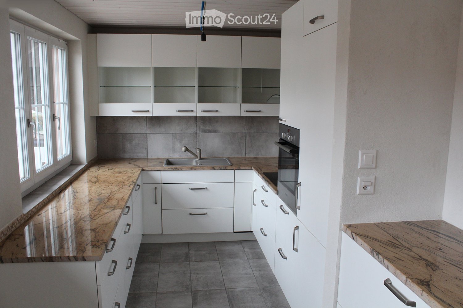 Modern kitchen with white cabinets, marble countertops, and stainless steel appliances including an oven and sink.