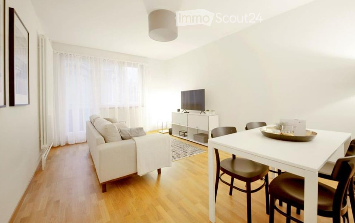 Bright living room with a white sofa, a dining table with chairs, a television on a white cabinet, and large windows with white curtains.