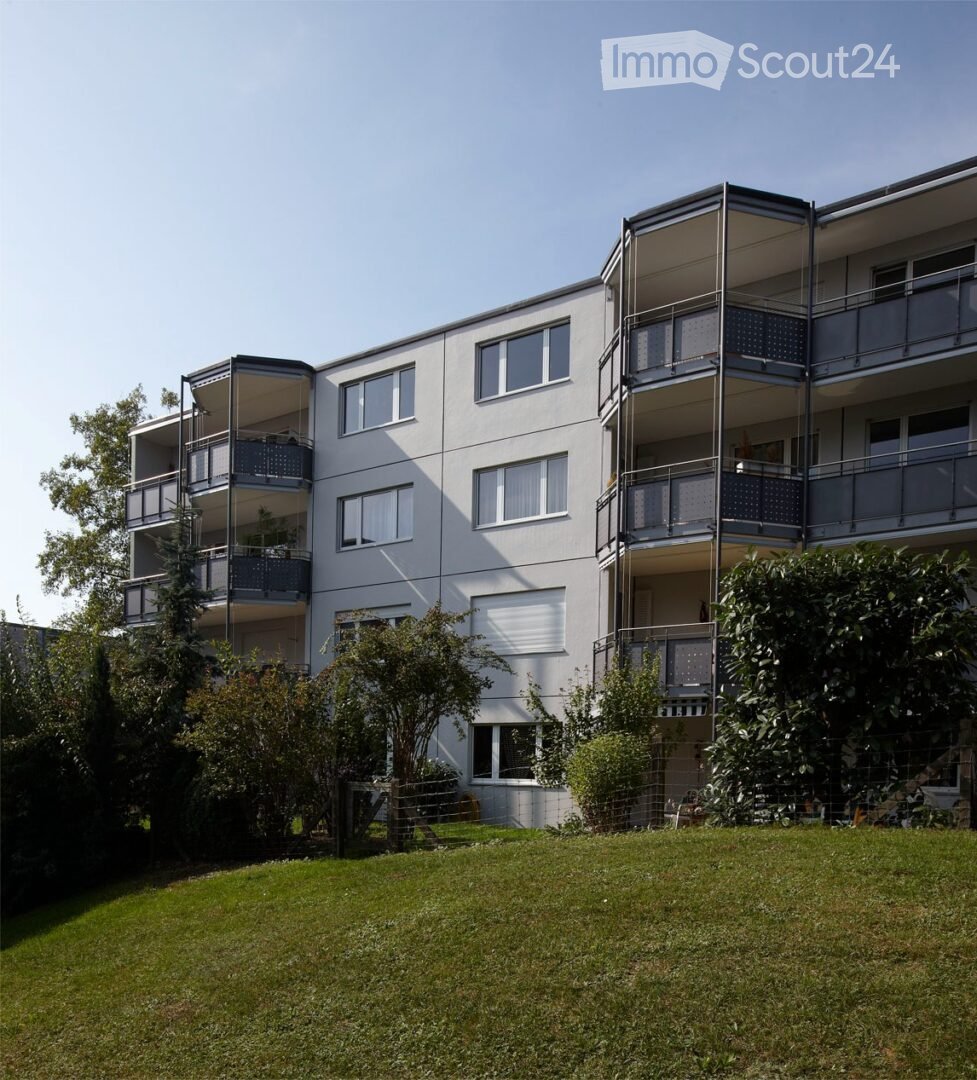 Modern multi-story apartment building with balconies, large windows, and surrounding greenery.