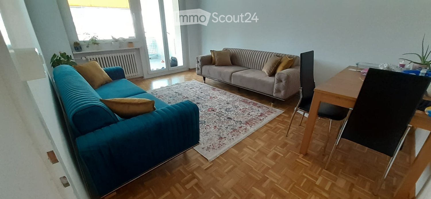 Living room with wooden flooring, two sofas, a dining table with chairs, and a patterned rug.