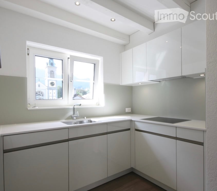 Modern kitchen with white cabinets, a sink, a stove, and large windows offering a view of a church tower.