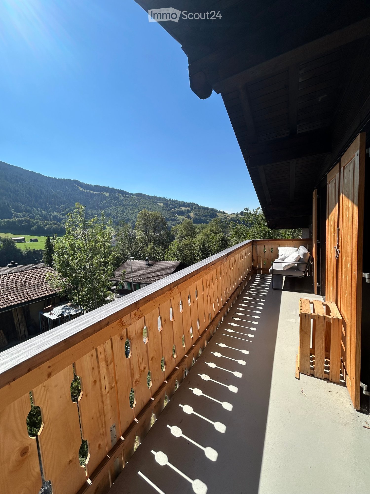 Wooden balcony with railing, overlooking a scenic mountain landscape, with a bench and chair.