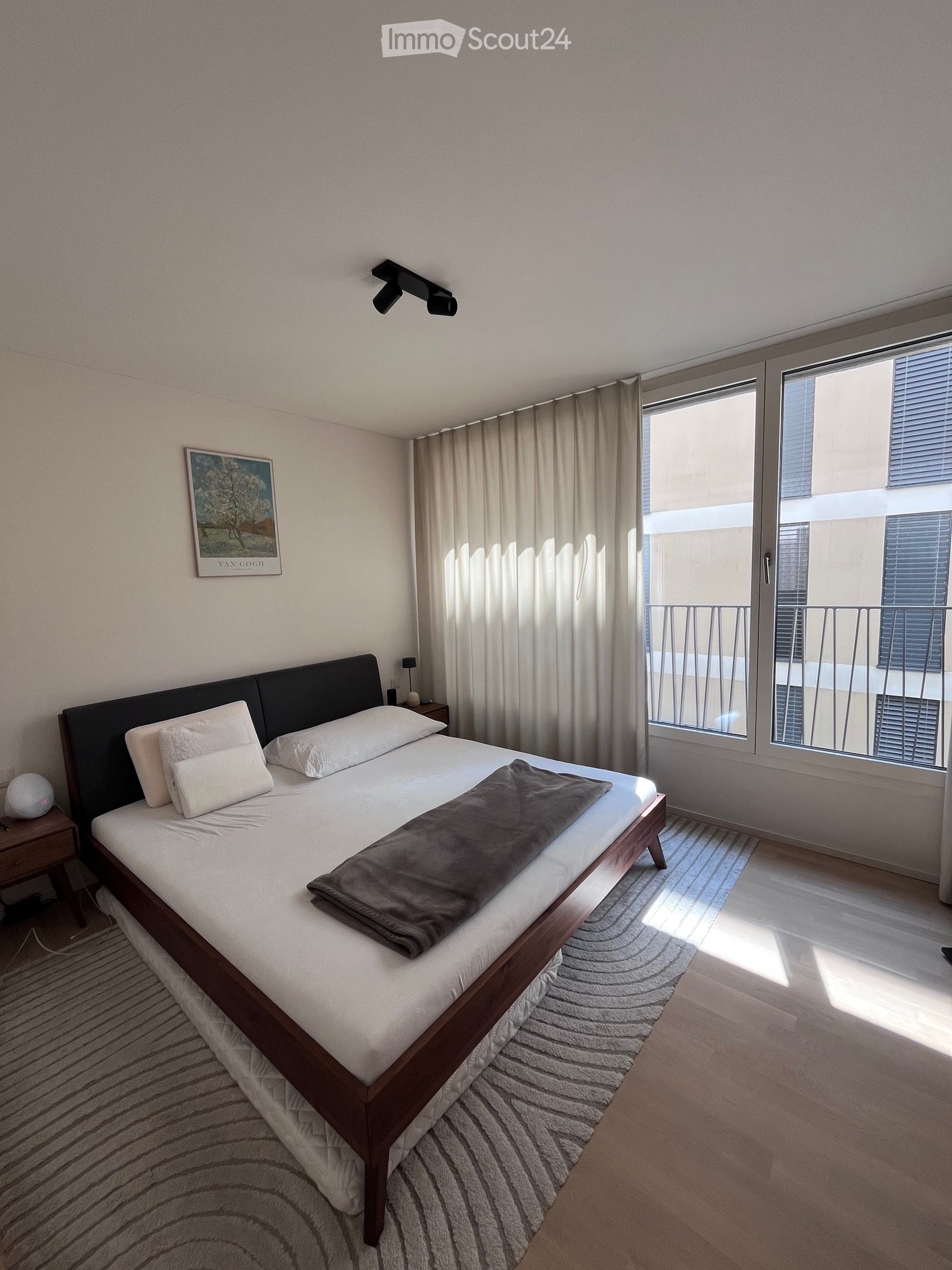 Modern bedroom with a double bed, nightstand, picture frame, and large window with curtains leading to a balcony.