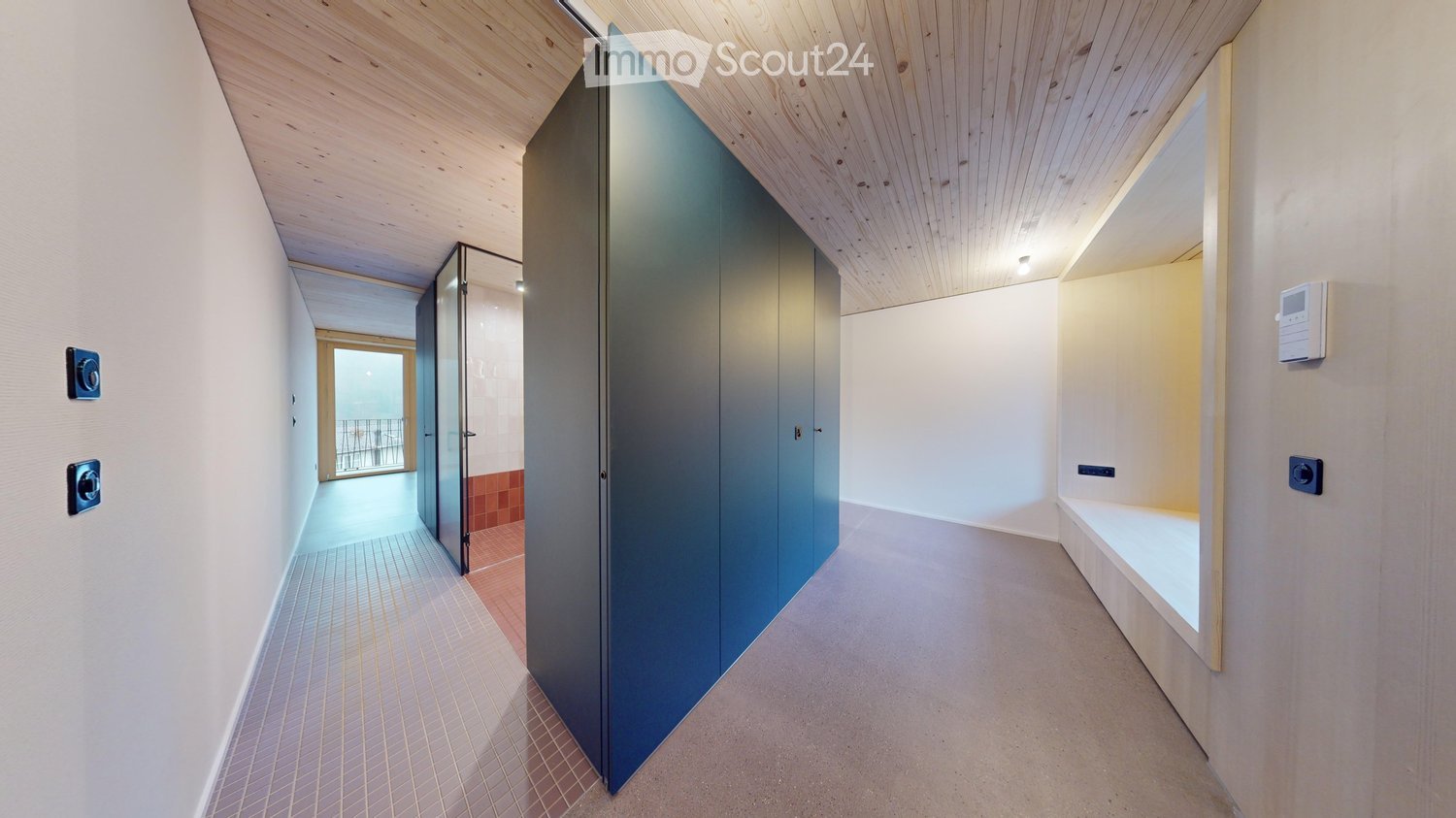 Modern hallway with light wooden ceiling, white walls, grey carpeted floor, and a large blue cabinet. A glass door leads to a balcony area with outdoor furniture visible.