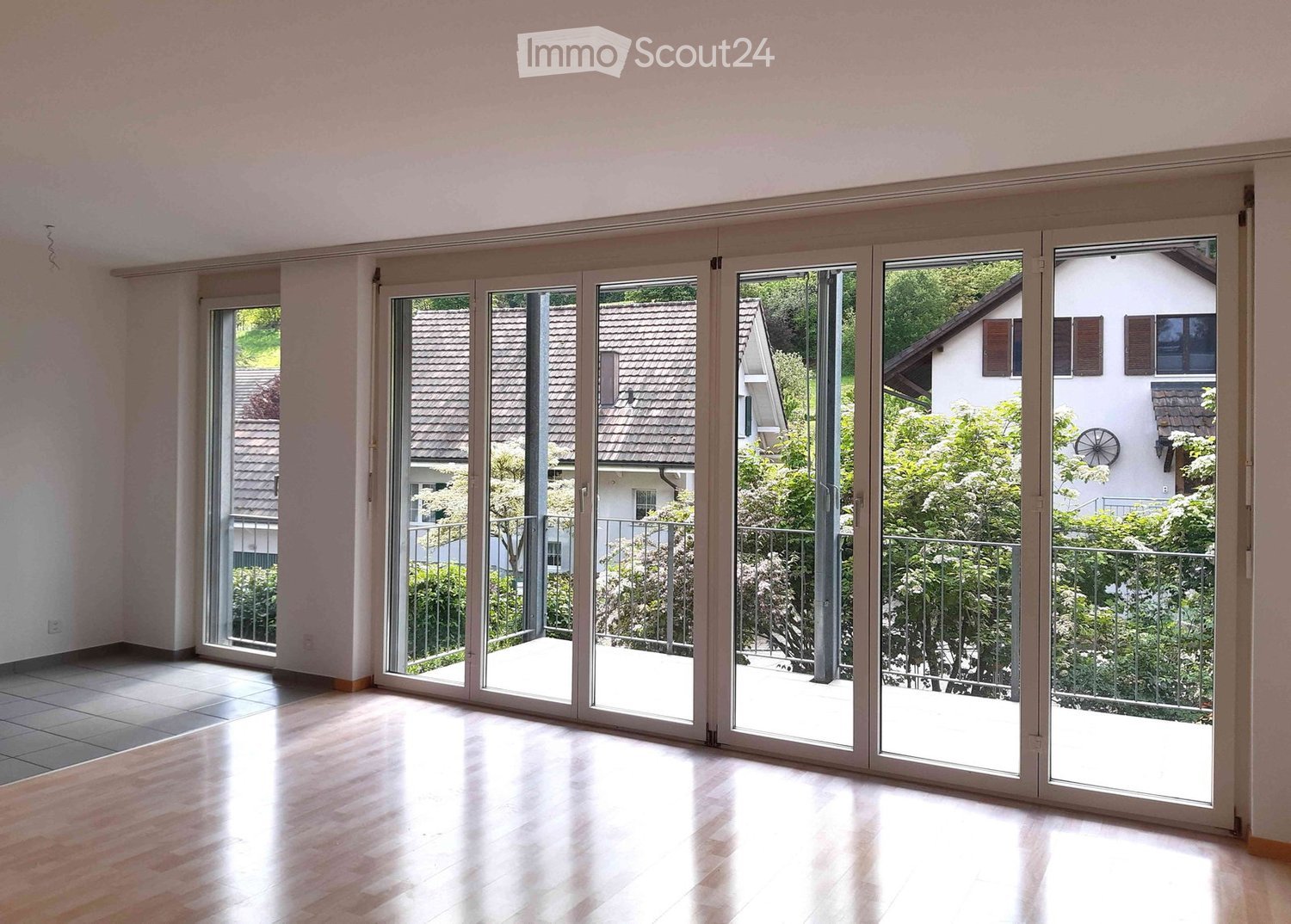 Bright, empty room with large sliding glass doors leading to a balcony, wooden flooring, and white walls.