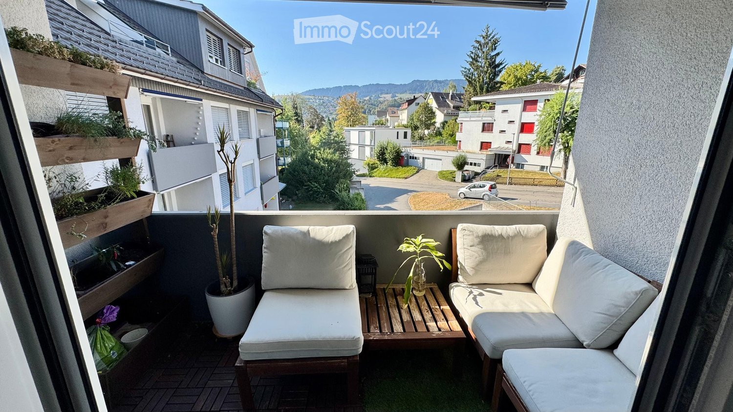 Balcony with a view of the neighborhood, featuring a small seating area with a sofa, table, and potted plants.