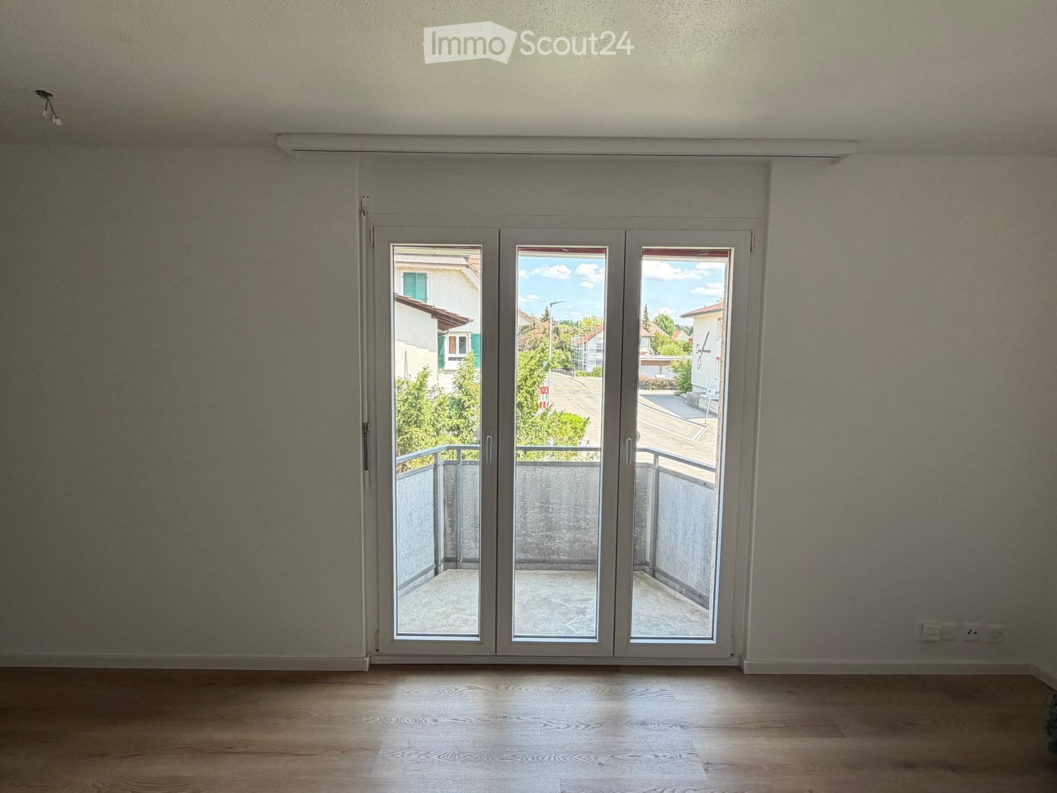 Empty room with wooden flooring, large sliding glass doors leading to a balcony, and neutral-colored walls.