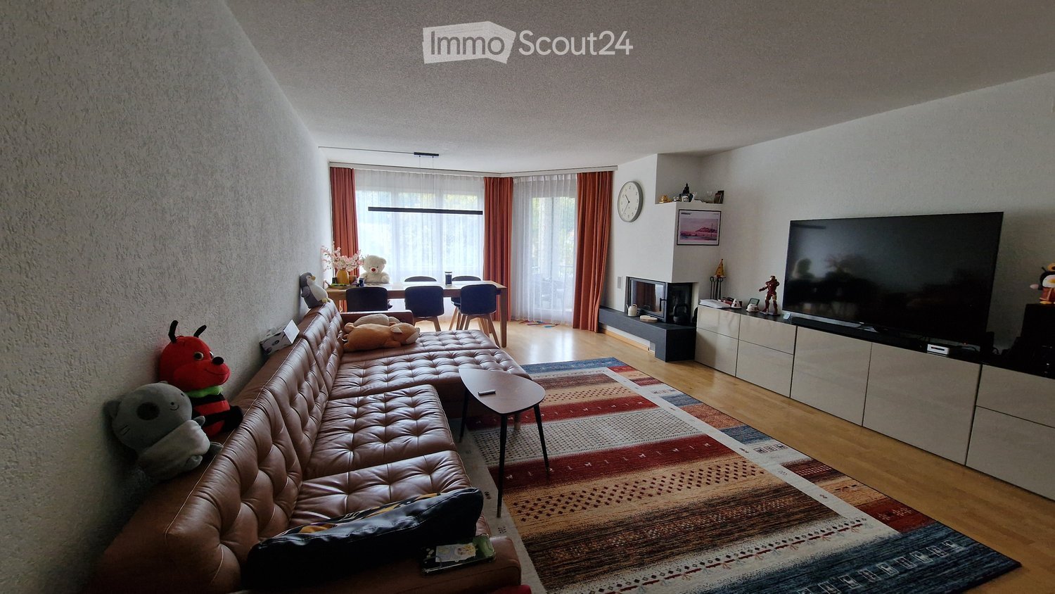 Modern living room with a leather sofa, coffee table, flat-screen TV, dining area with chairs, fireplace, and decorative items.