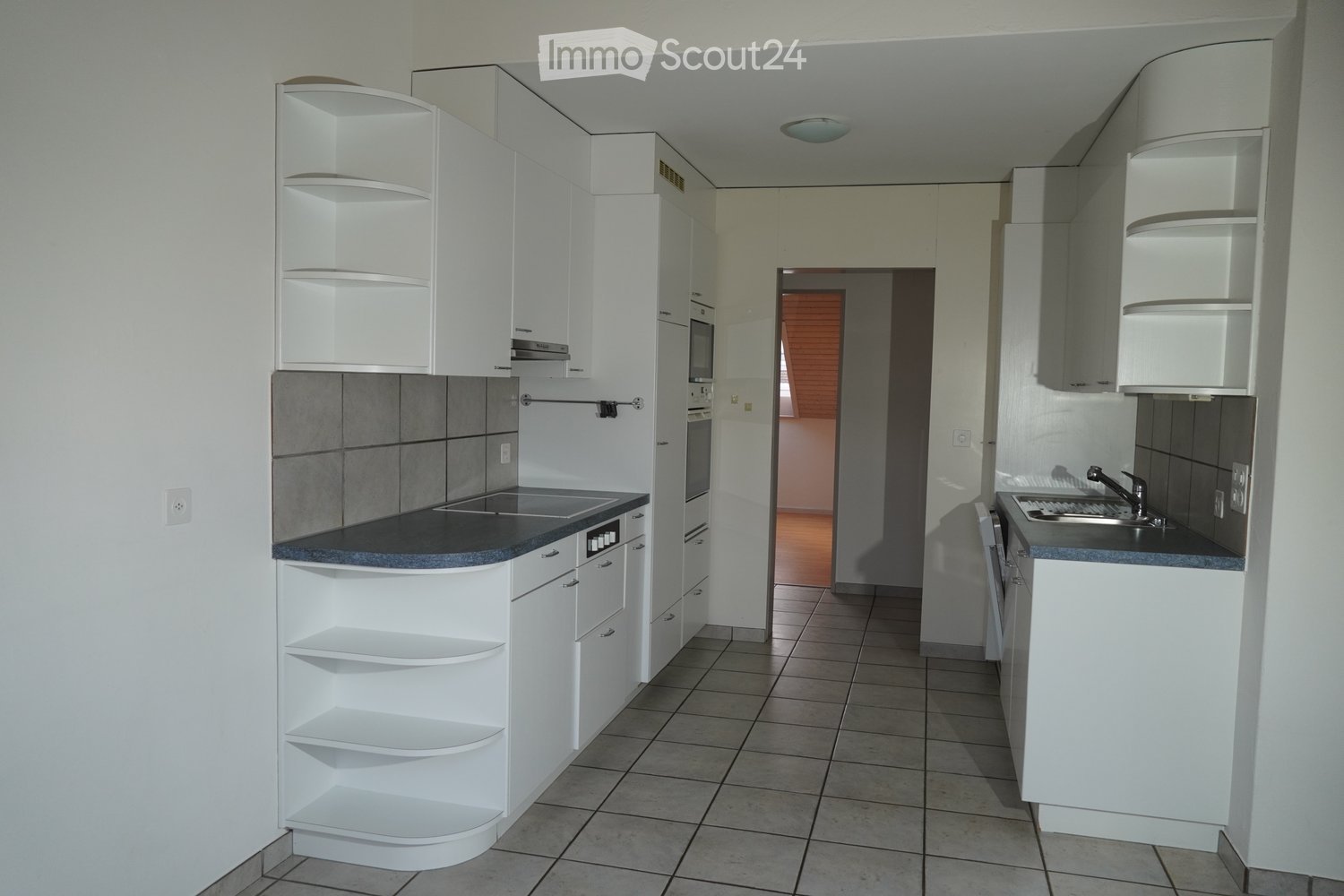 Modern kitchen with white cabinets, gray tiled backsplash, and a black countertop. Features include a sink with a faucet, an oven, and a microwave.