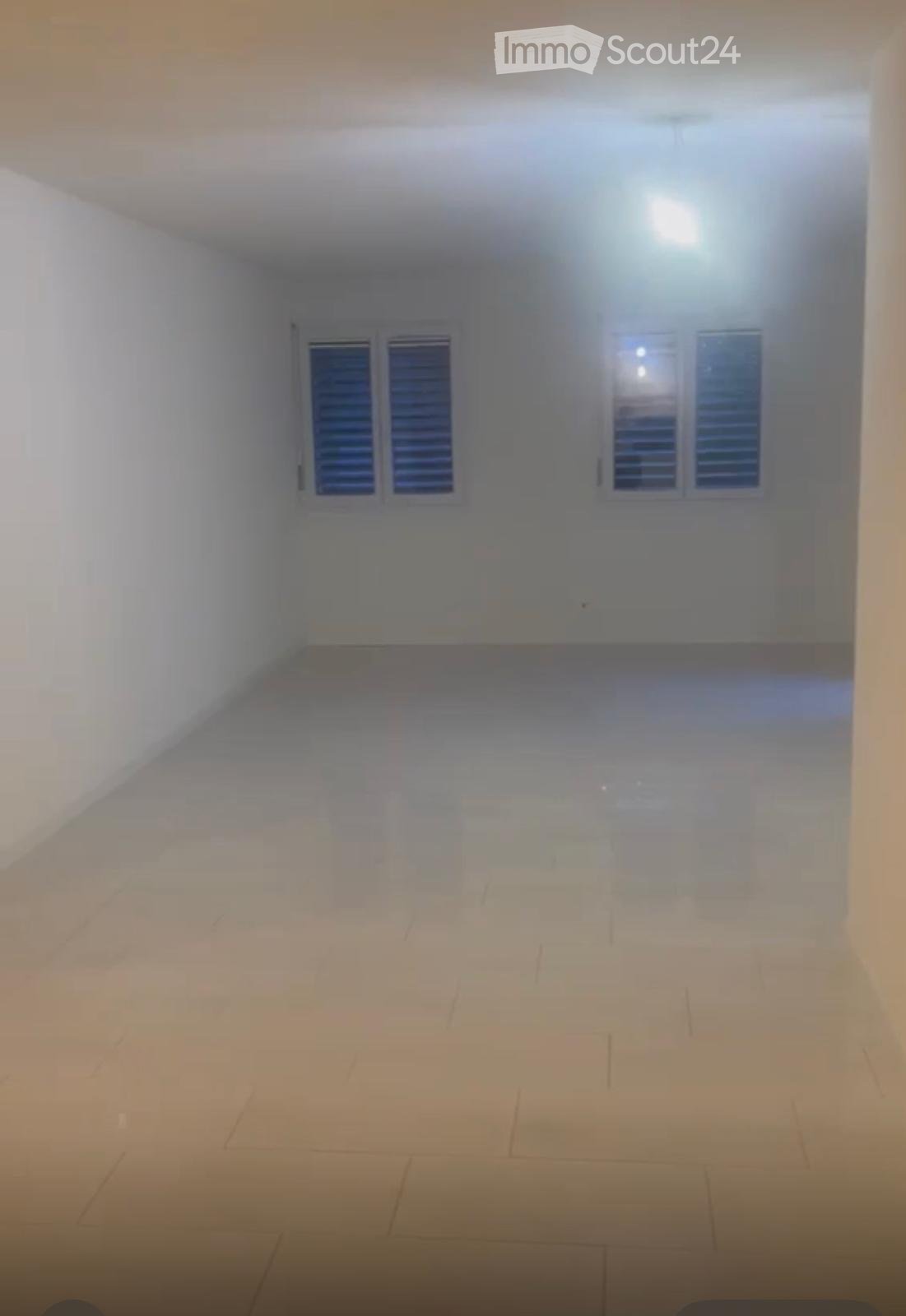 Empty room with white walls, tiled floor, and two windows with shutters.