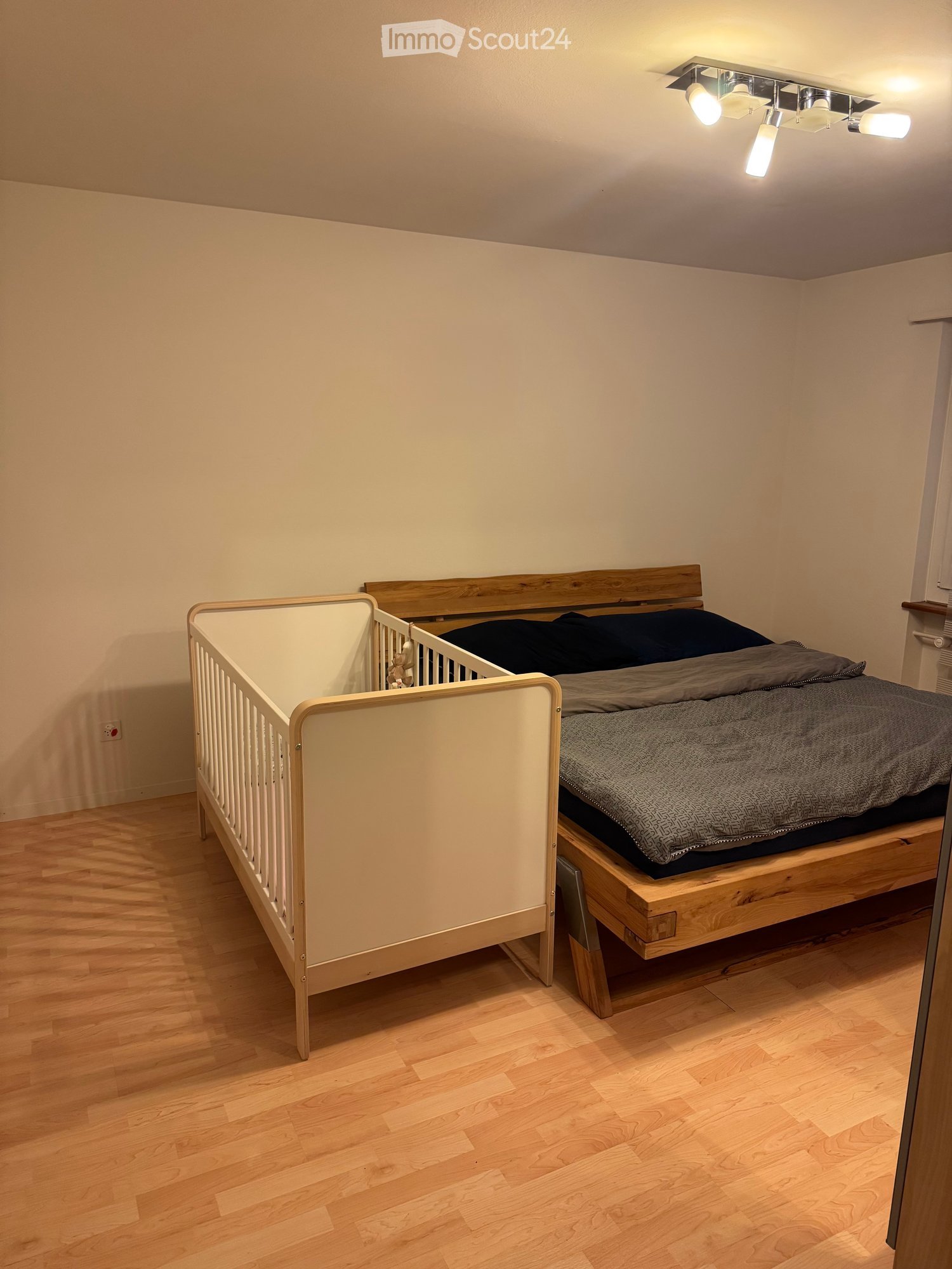 Cozy bedroom with wooden flooring, a single bed with dark bedding, and a small crib next to it.