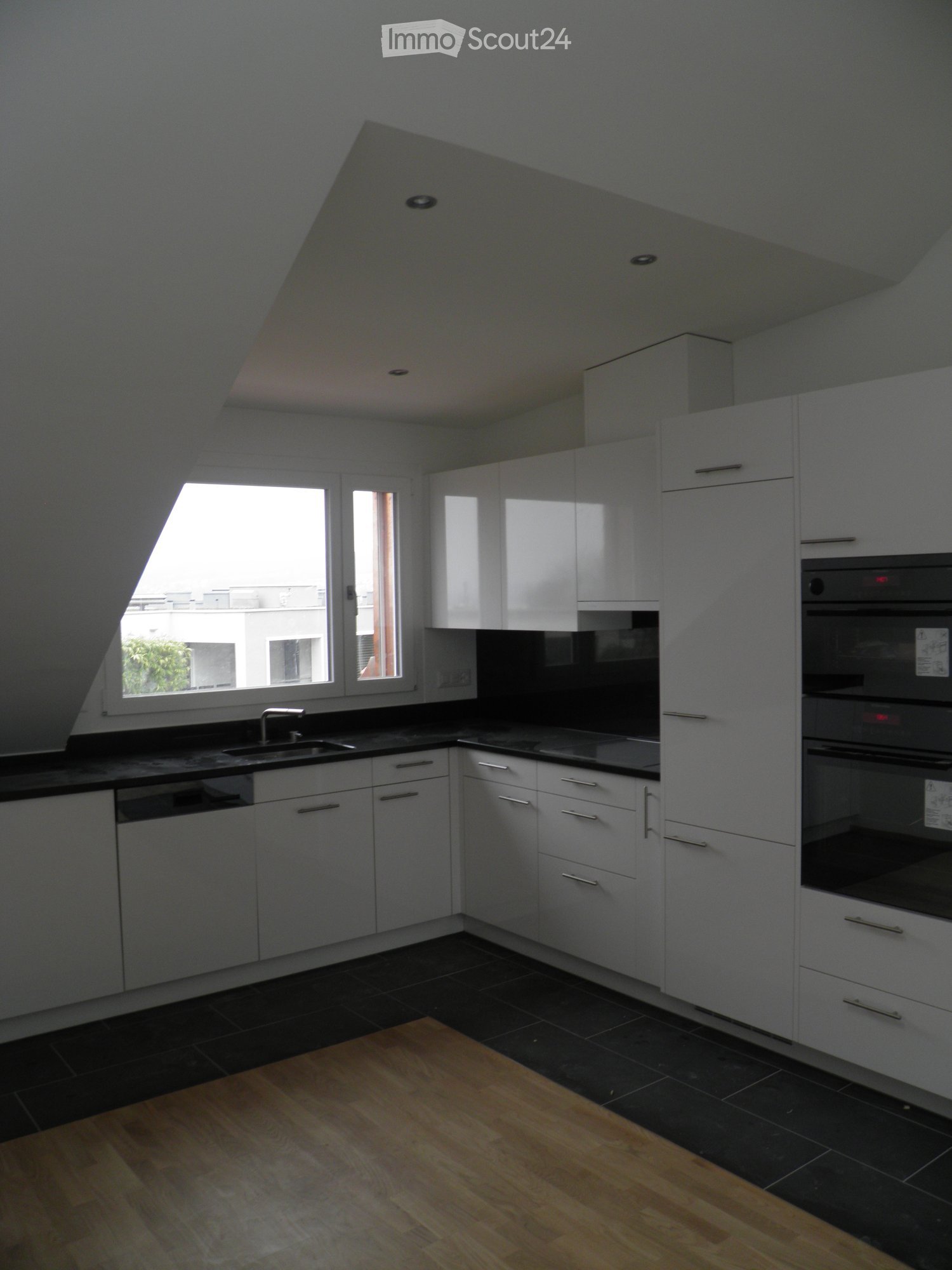 Modern kitchen with white cabinets, black countertops, and a wooden floor. Features a sink, faucet, oven, and dishwasher.