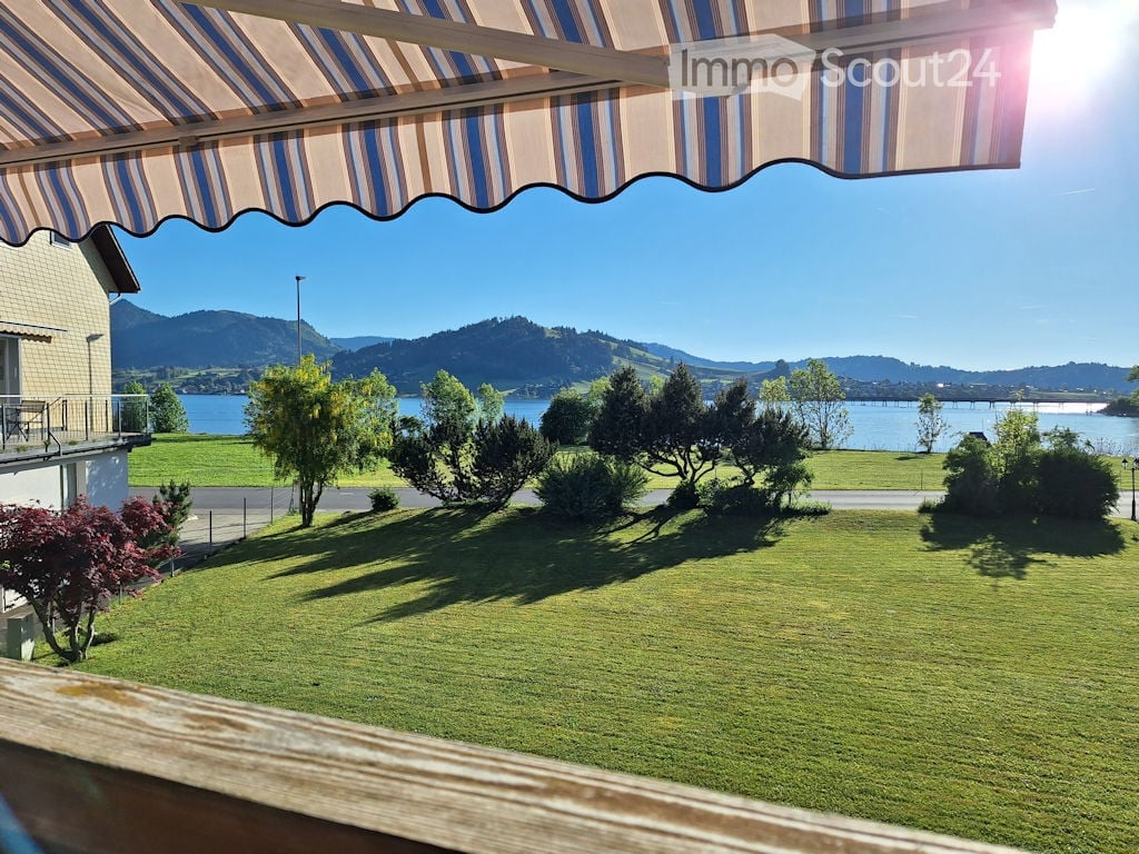 Lush green lawn with trees and shrubs, overlooking a lake and distant mountains under a clear blue sky.
