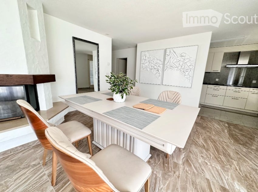 Modern dining area with a white dining table, four chairs, a potted plant, a fireplace, and artwork on the wall.