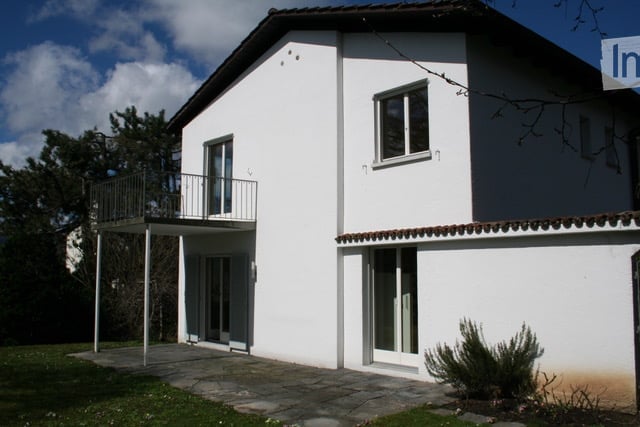 Two-story white house with a balcony, large windows, and a tiled roof.