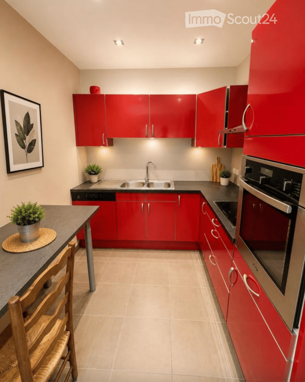 Modern kitchen with red cabinets, stainless steel appliances, and a small dining area with a table and chairs.