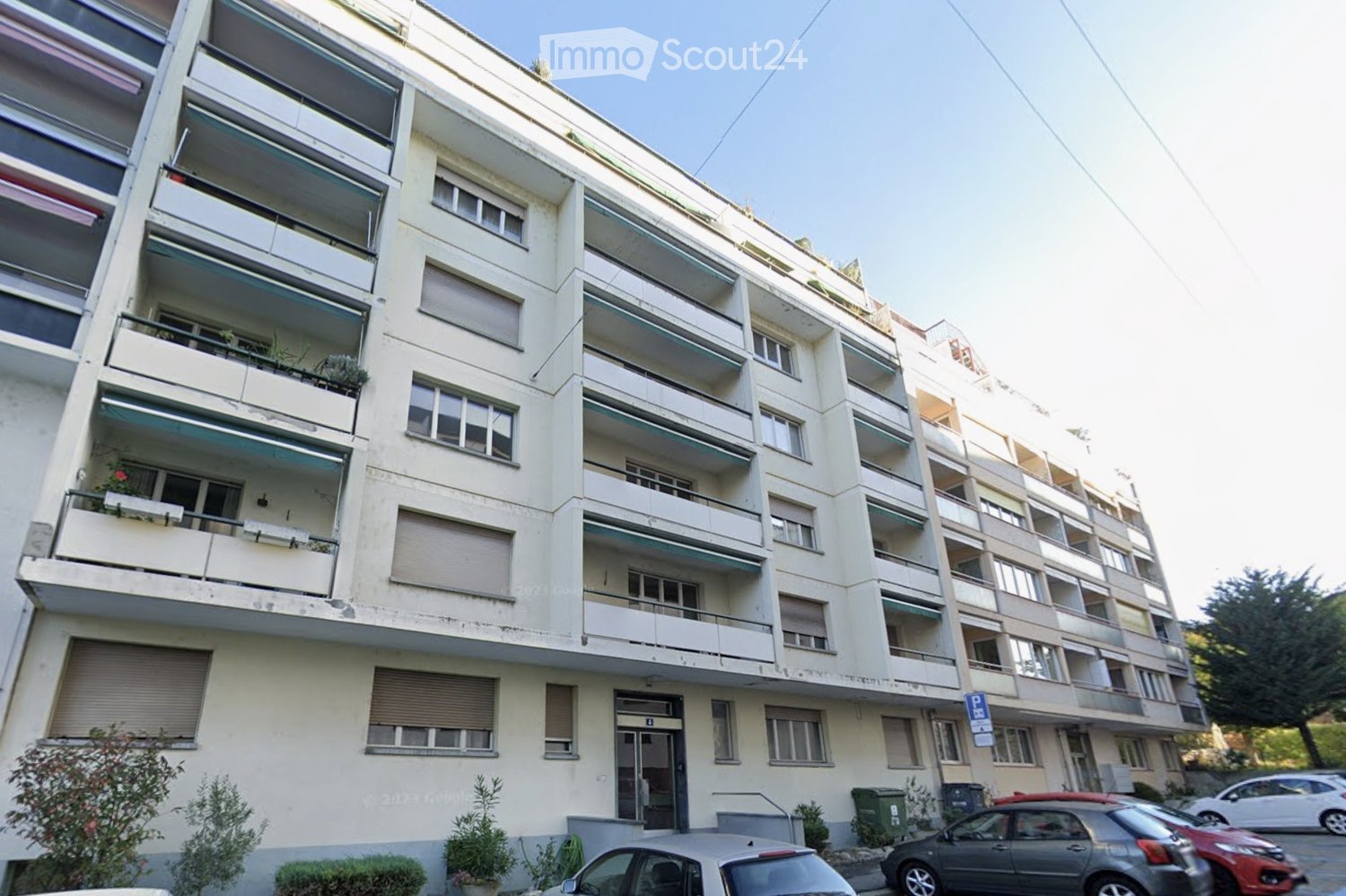 Multi-story residential building with balconies, windows, and parked cars in front.